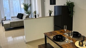 A modern living room with a sofa, a dining table set with plates and glasses, and a TV mounted on the wall. - C&V: 3 PP - 2 rooms +WLAN+Smart-TV+Boxspringbed (Kaiserslautern)