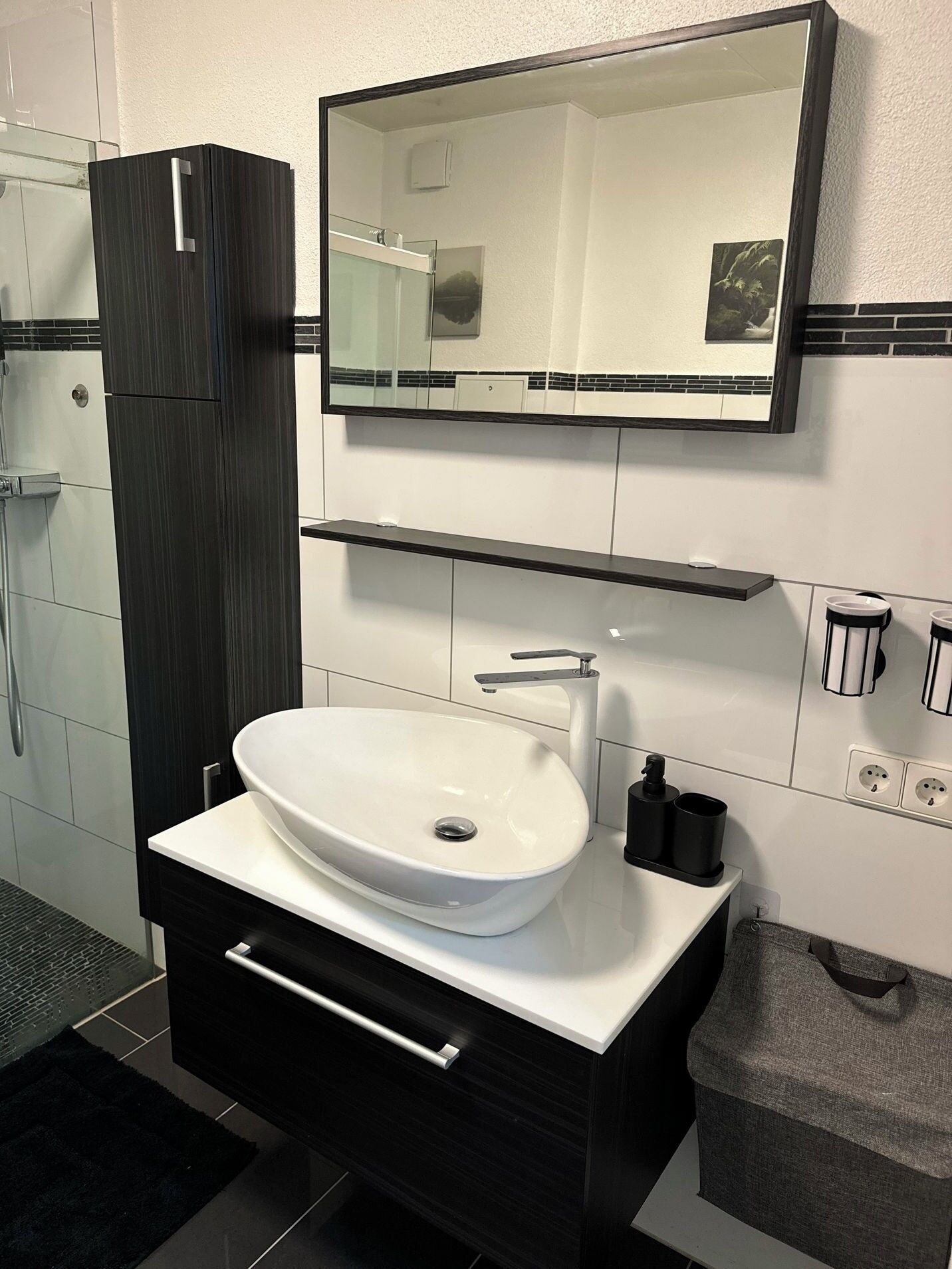 Ein modernes Badezimmer mit einem weißen Waschbecken, dunklen Schränken und einem großen Spiegel über dem Waschtisch.