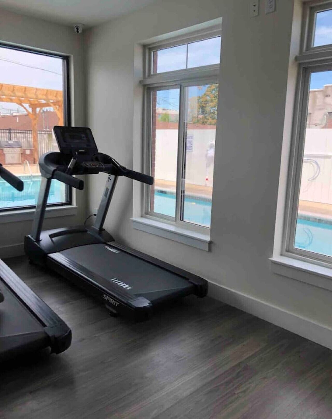 Une salle de sport à domicile équipée d’un tapis de course et d’un vélo d’appartement, avec de grandes fenêtres et une vue sur une piscine.