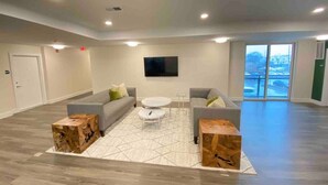 A spacious living room with a grey sofa, two white coffee tables, and a large window with a view of a snowy landscape. - Modern Penthouse Condo with Panoramic City View (Nashville)