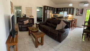 A living room with a leather sofa, a wooden coffee table, a TV, and a kitchen in the background. - Gorgeous Poolside Apartment (Pajonal)