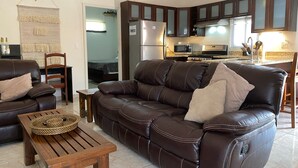 A living room with a brown leather sofa, a wooden coffee table, and a wall-mounted macrame piece. - Gorgeous Poolside Apartment (Pajonal)