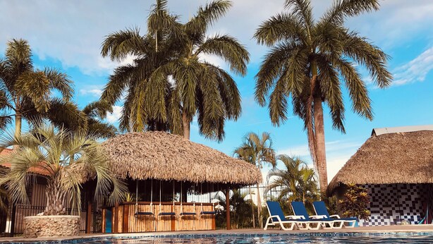 A pool area with lounge chairs and thatched-roof structures. - Gorgeous Poolside Apartment (Pajonal)