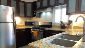 A kitchen with dark wooden cabinets, a stainless steel refrigerator, a microwave, a stove, and a sink. - Gorgeous Poolside Apartment (Pajonal)