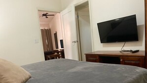 A bedroom with a bed, a desk, a chair, a television, and a ceiling fan. - Gorgeous Poolside Apartment (Pajonal)