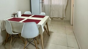 Un coin repas avec une table dressée pour quatre personnes, des chaises blanches, un réfrigérateur blanc et un tableau accroché au mur.