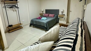 Une chambre à coucher avec un lit, un téléviseur fixé au mur, une étagère avec des vêtements et une petite table avec une lampe.