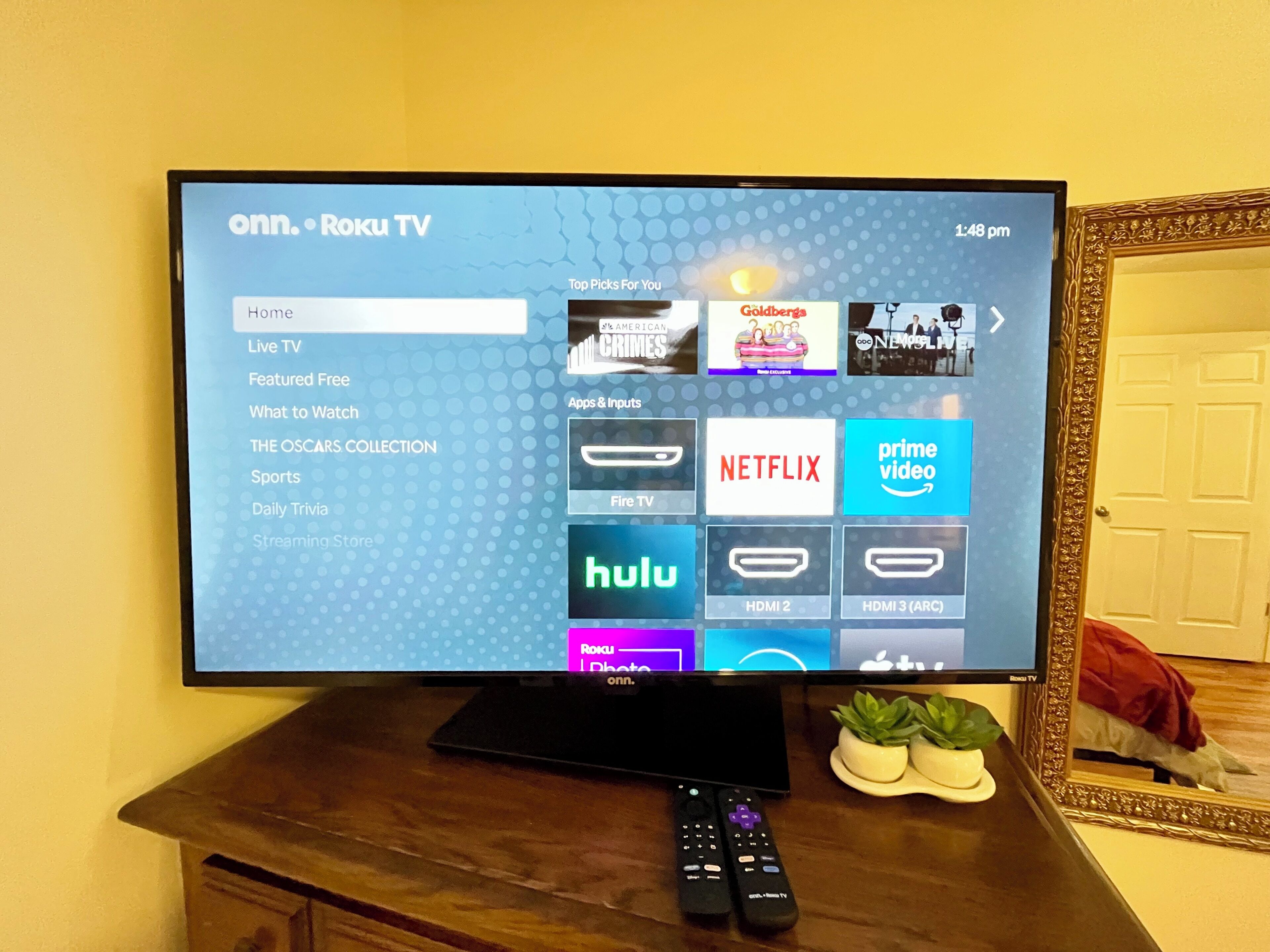 En Roku-tv som visar en startsida med olika streamingtjänster, och en fjärrkontroll ligger på ett träbord.