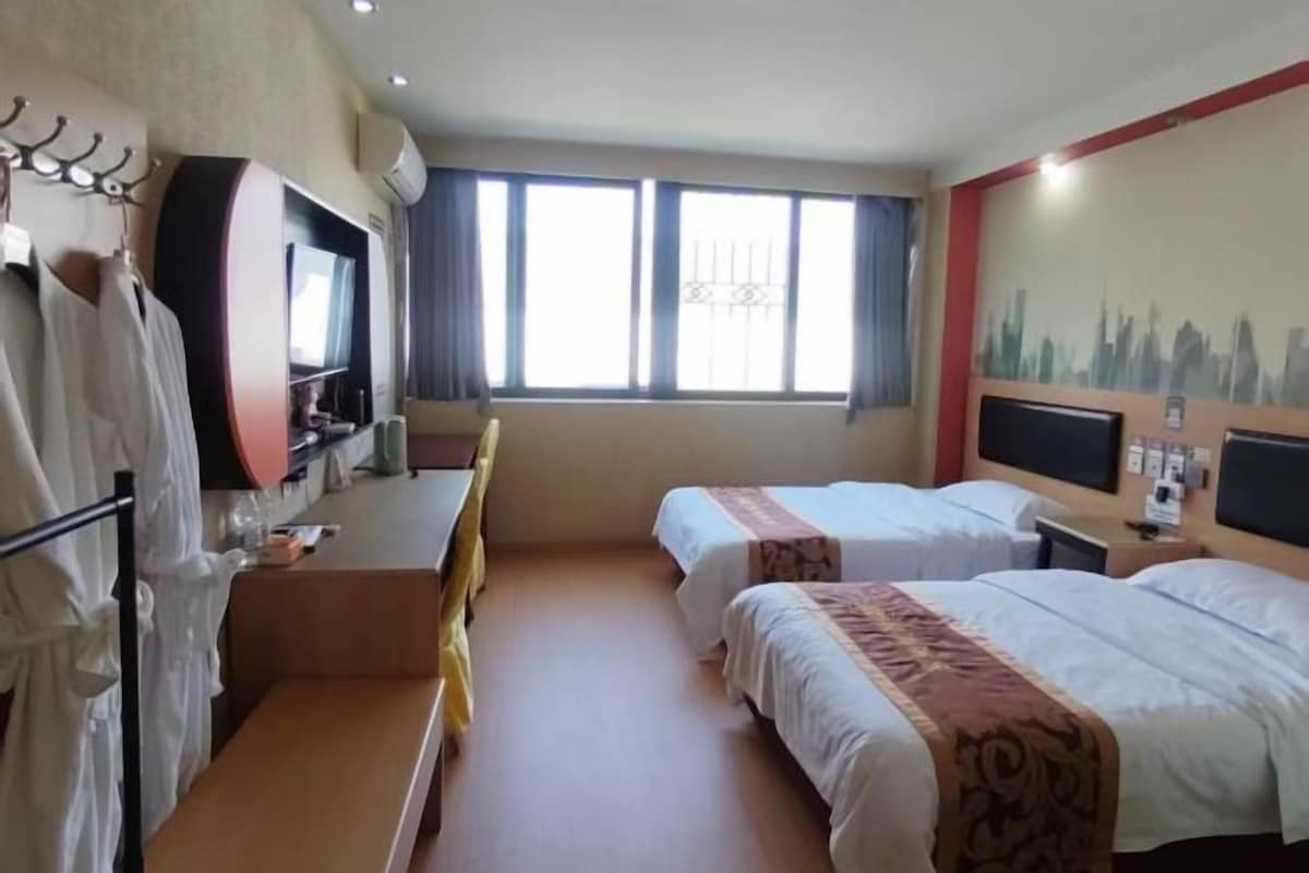 A hotel room with two beds, a desk, a TV, and a cityscape mural.