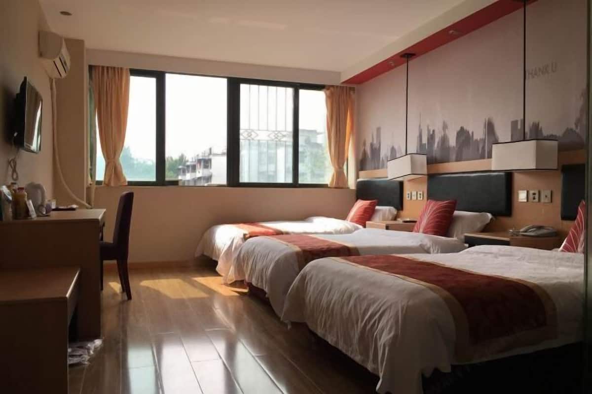 A hotel room with two beds, a desk, a chair, a TV, and a cityscape mural on the wall.