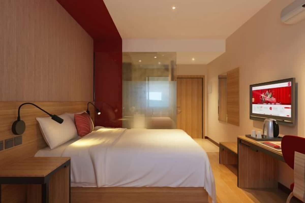 A modern hotel room with a bed, bedside table, and a desk with a chair.