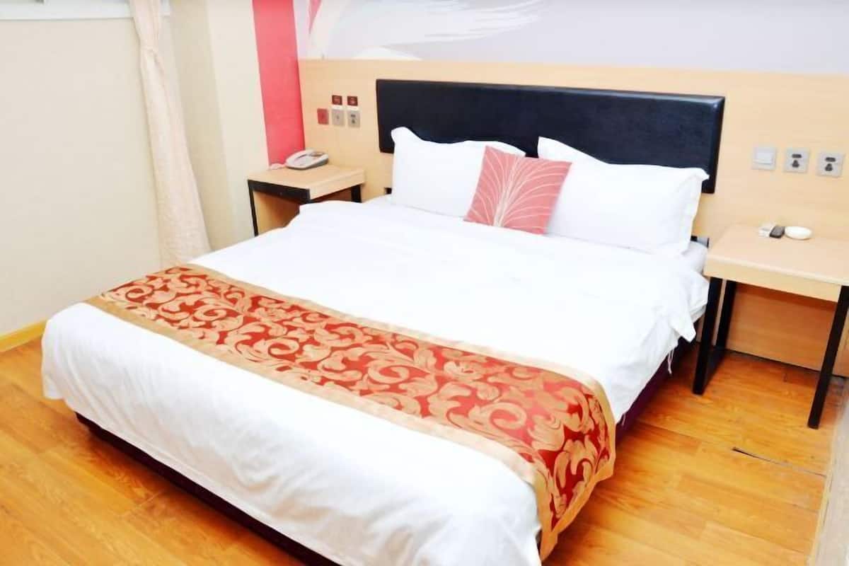 A hotel room with a large bed, a bedside table with a phone, and a nightstand.