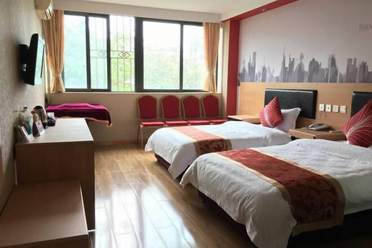 A hotel room with two beds, a desk, a chair, a TV, and a cityscape mural.