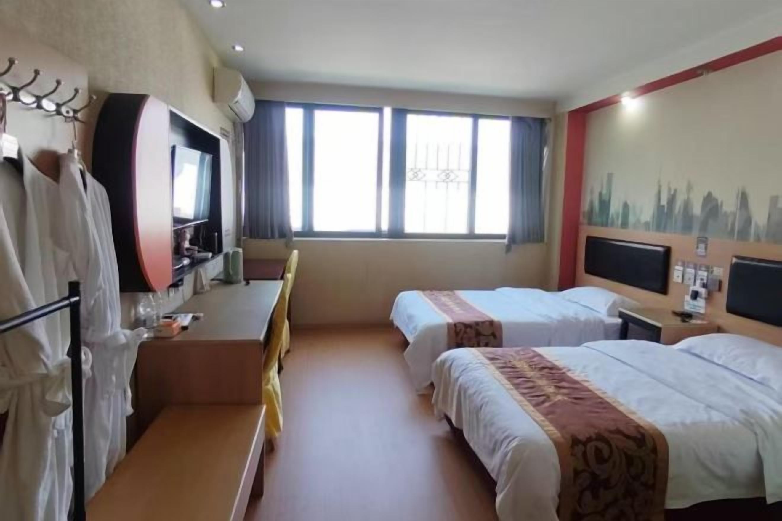 A hotel room with two beds, a desk, a TV, and a cityscape mural.