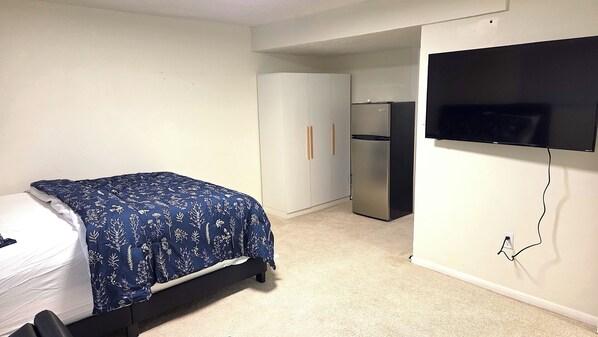 Un dormitorio con cama, armario, refrigerador y televisor.