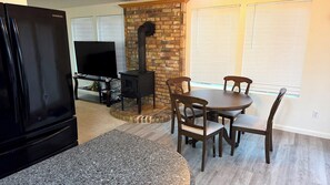 Una sala de estar con un refrigerador negro, un televisor sobre un mueble, una chimenea y una mesa de comedor con sillas.