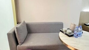A modern room with a grey sofa, a round marble table with water bottles, a tray with cups, and a vase. - Lavande Hotel (Beijing)