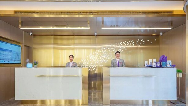 A hotel reception area with two reception desks, a digital screen, and a decorative wall feature. - Lavande Hotel (Beijing)