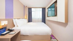 A hotel room with a bed, bedside table, lamp, and a TV mounted on the wall. - Lavande Hotel (Beijing)
