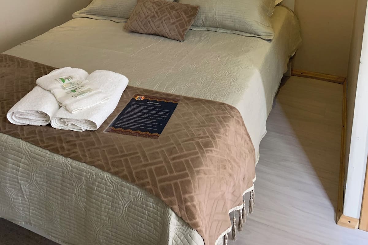 A neatly made bed with a brown headboard and beige bedding, a folded white towel, and a small informational card on the bed.