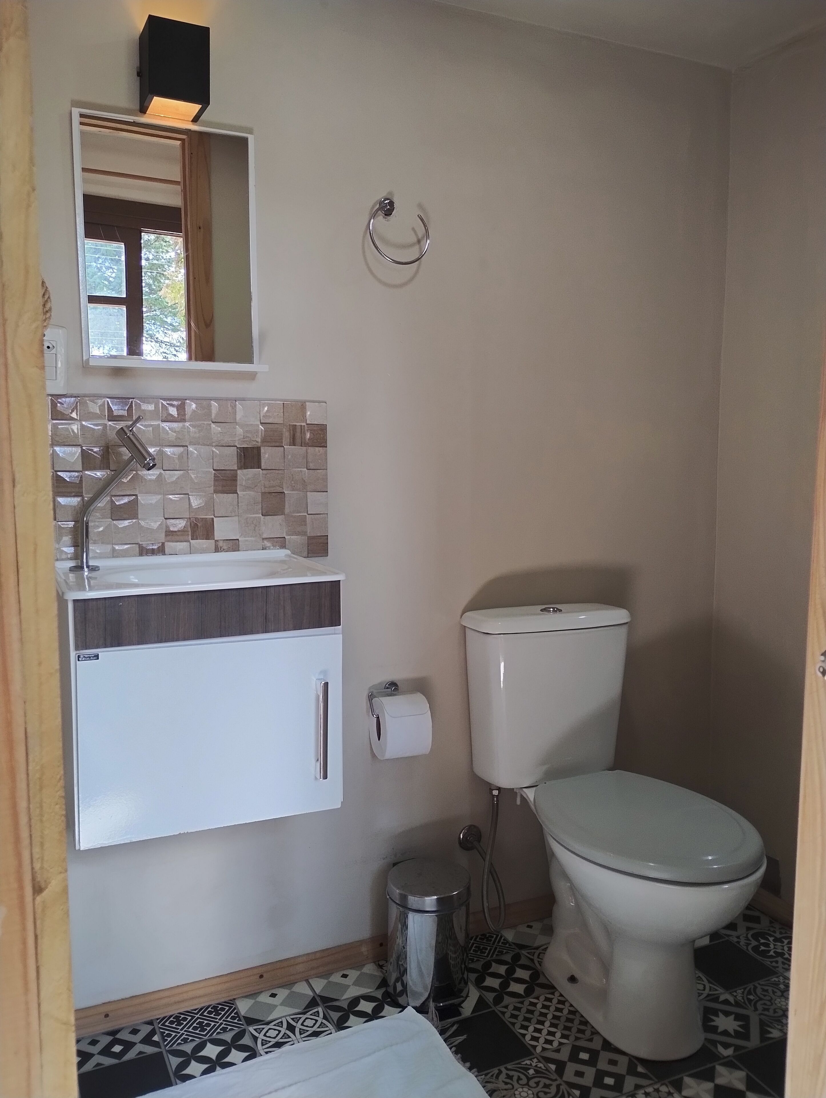 Un baño pequeño con inodoro, lavamanos con espejo y un cubo de basura.