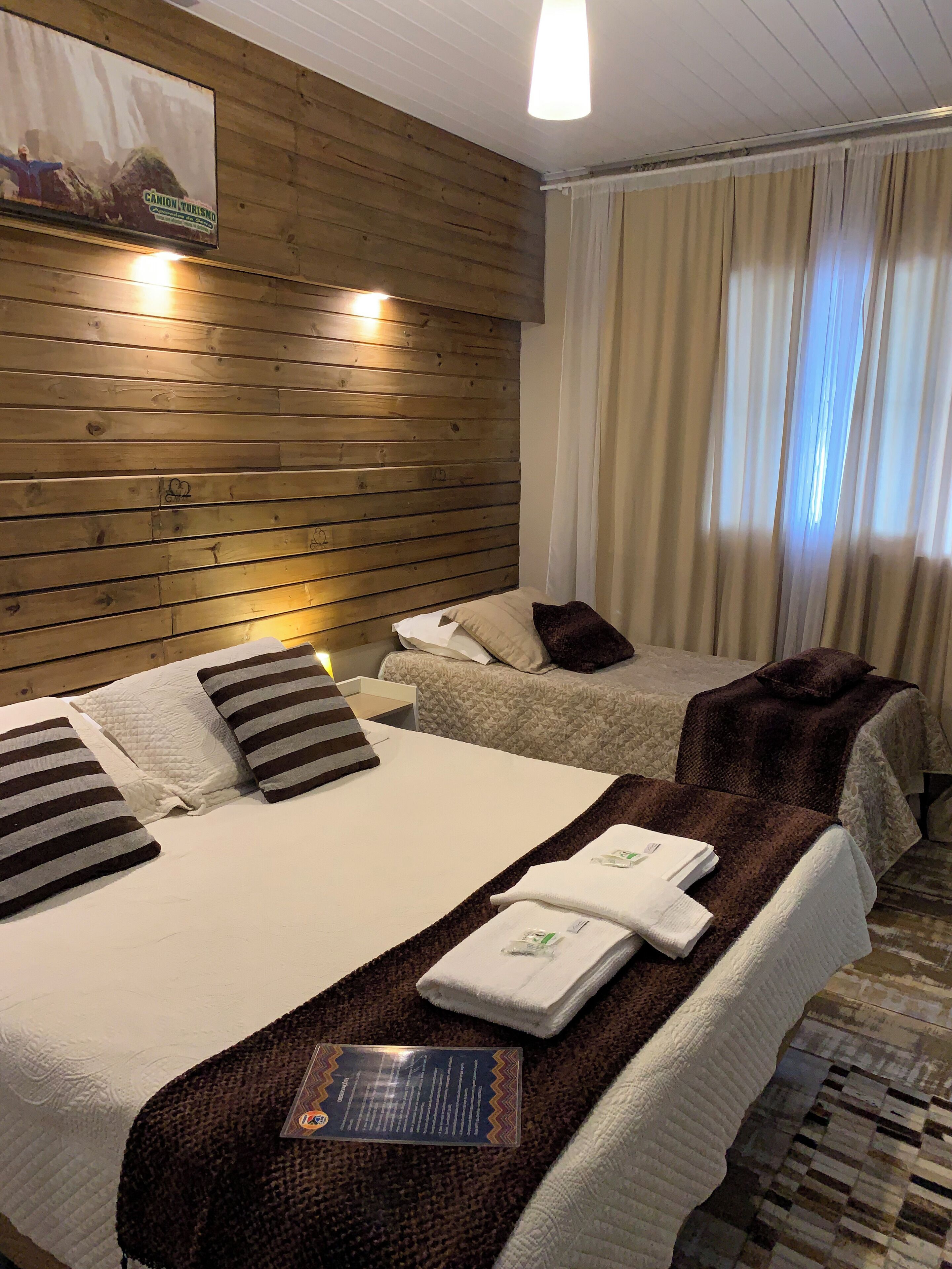 Habitación de hotel con dos camas, paneles de madera en las paredes, un ventanal con cortinas y un cartel en la pared.
