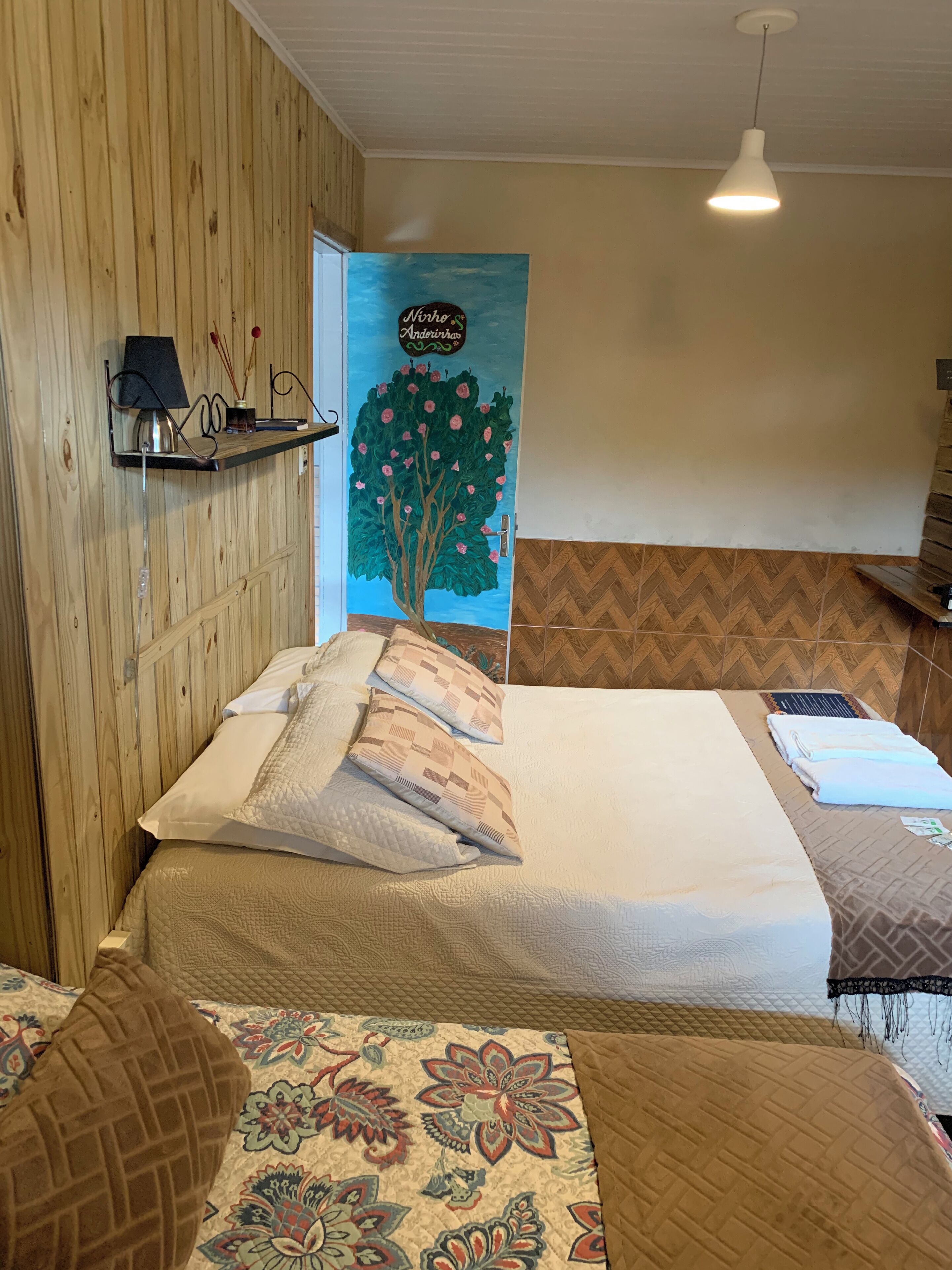 A hotel room with two beds, a wooden wall, a mural, and a hanging lamp.