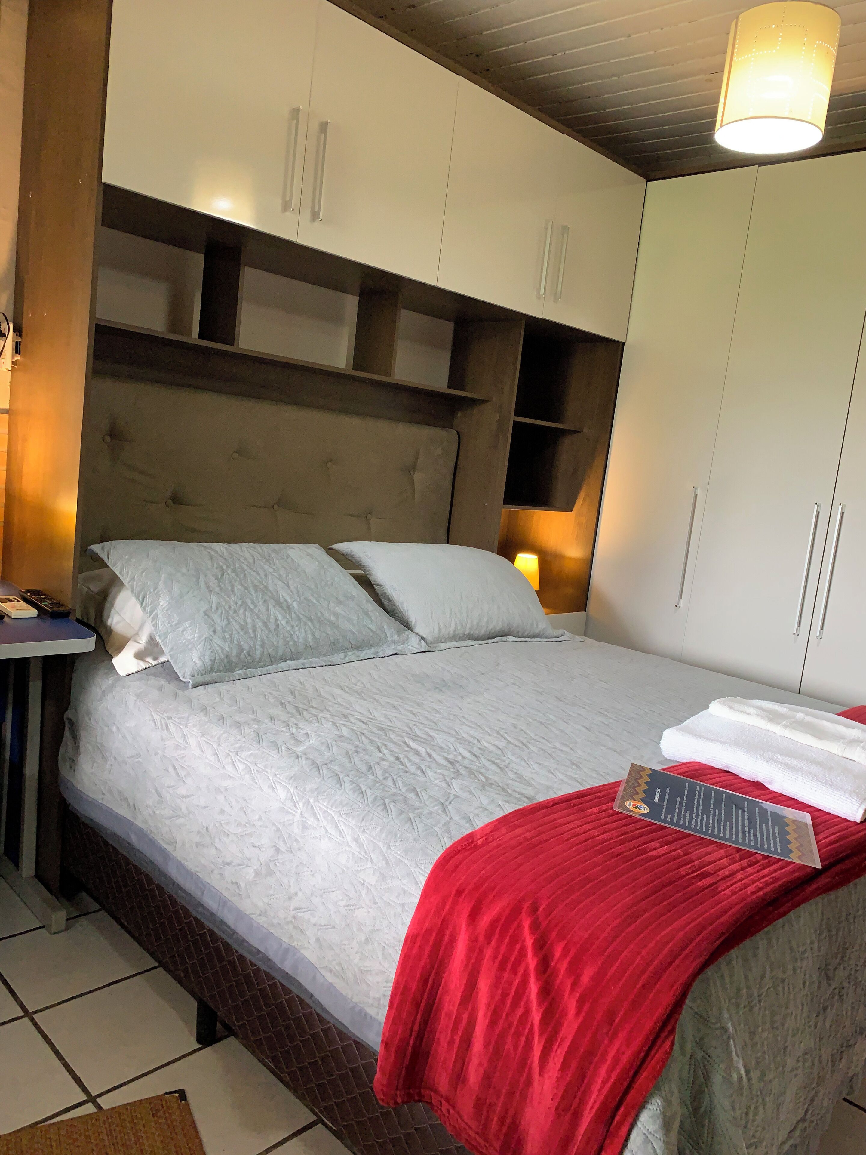 Un dormitorio con cama, mesita de noche, manta roja y toalla blanca.