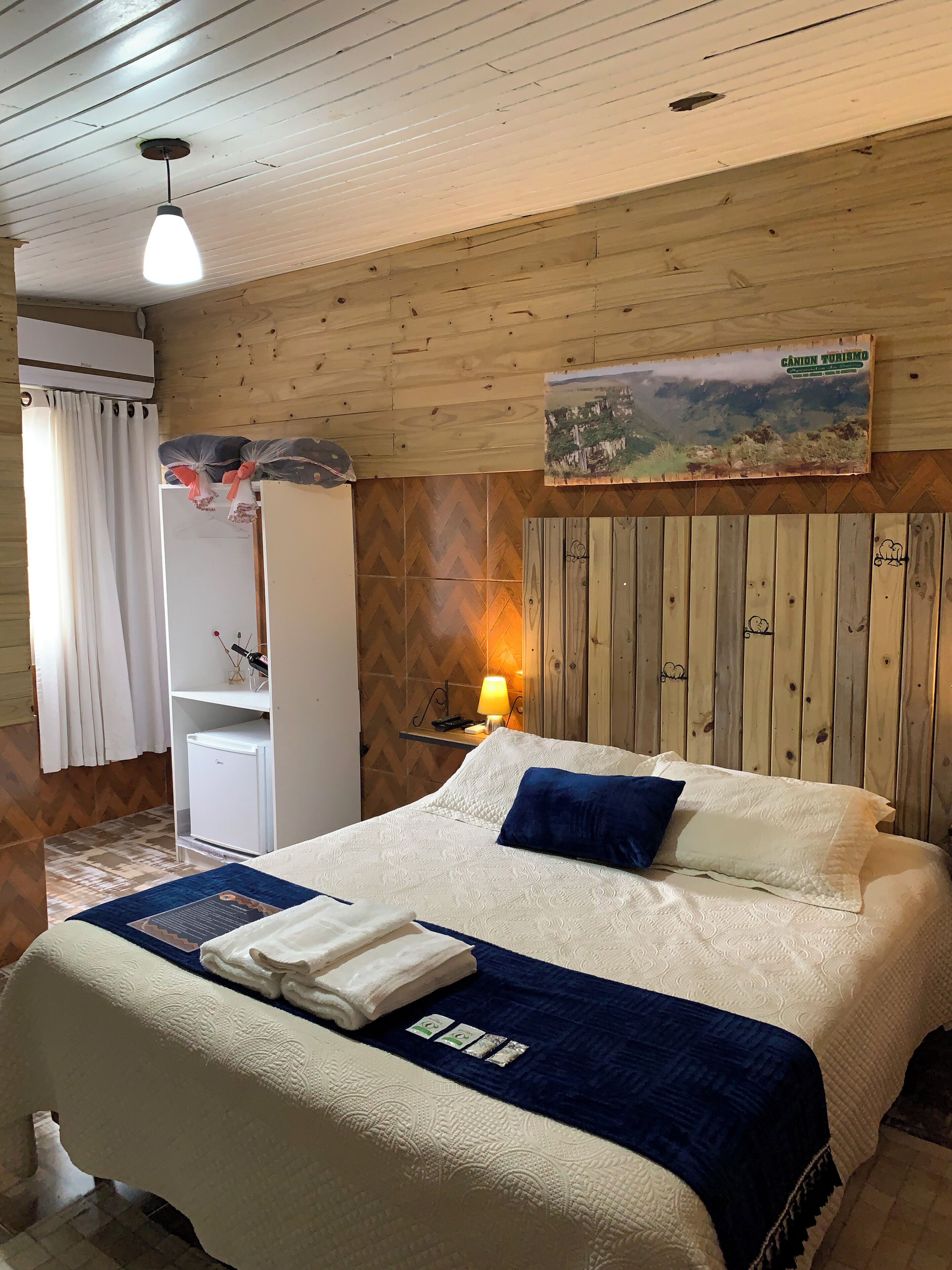Een hotelkamer met een bed, een bureau, een stoel, een lamp en een schilderij aan de muur.