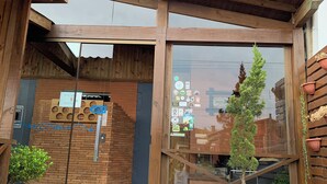 A wooden building with a glass entrance, a wooden deck, and a small tree in a planter. - Pousada Deck 950 (Cambará do Sul)