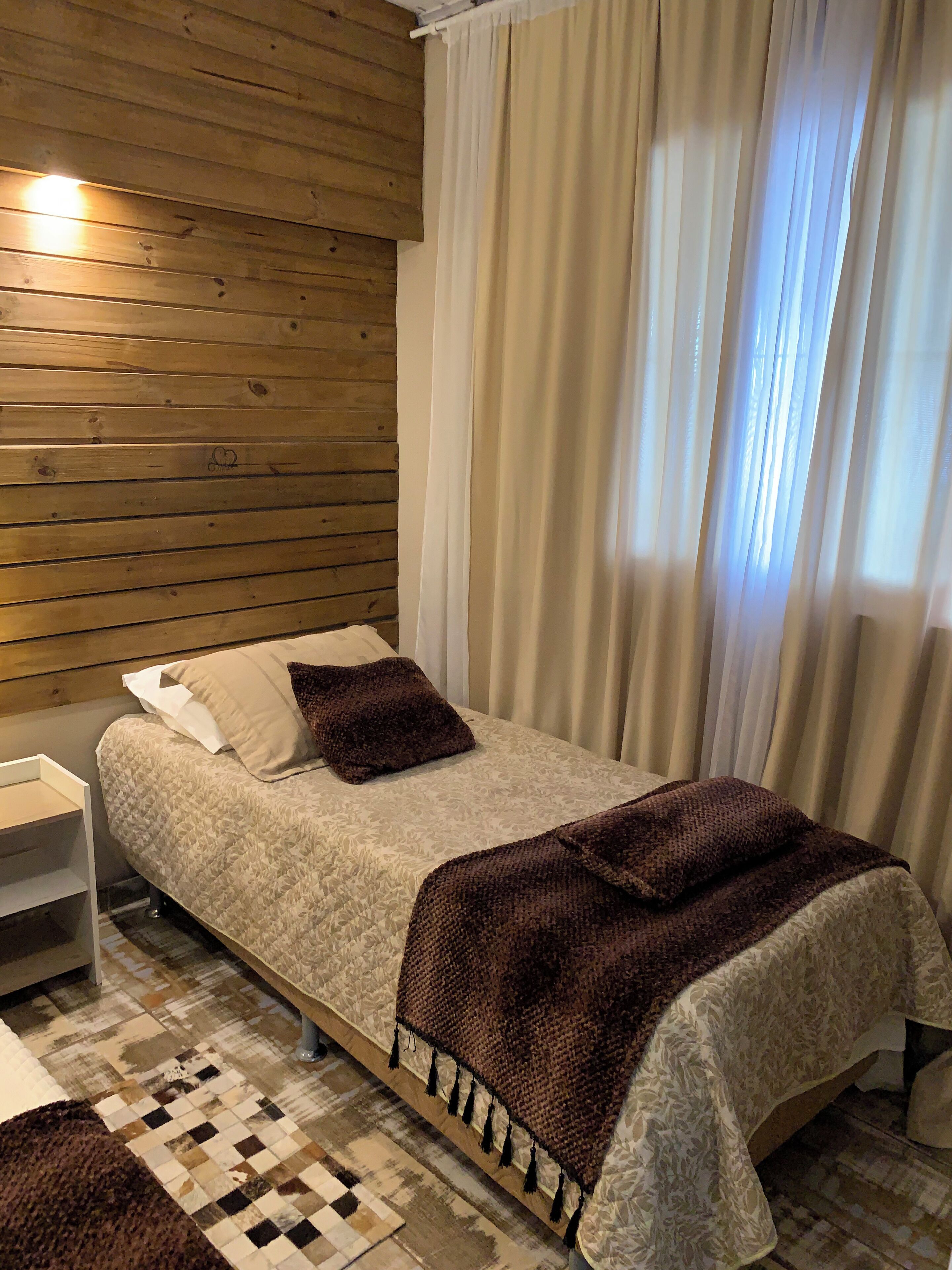 Una habitación con una cama, una mesita de noche, un tapete estampado y una pared de madera.