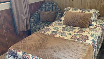 Una habitación con cama, una silla, una cortina y pared de madera.