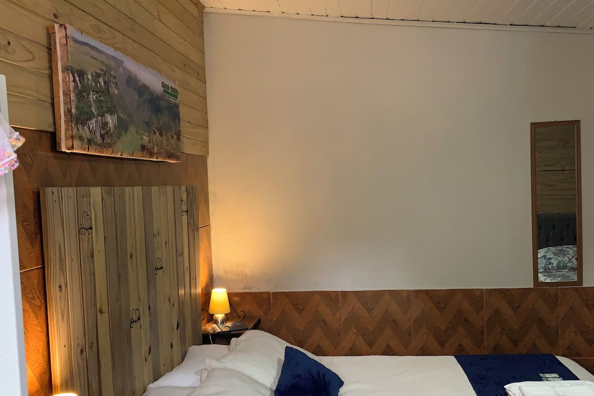 A hotel room with a wooden headboard, a bed with white bedding and a blue throw, a nightstand with a lamp, and a painting on the wall.
