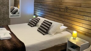 A neatly arranged bedroom with a wooden headboard, a bed with striped pillows, a bedside table with a lamp, and a mirror on the wall. - Pousada Deck 950 (Cambará do Sul)