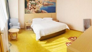 A hotel room with a bed, a chair, a small table, and a painting on the wall. - Vienna Hotels Zao Zhuang QingTAN Road (Zaozhuang)