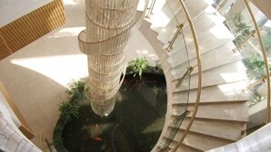 A modern atrium with a central water feature, a spiral staircase, and a glass ceiling allowing natural light. - Vienna Hotels Zao Zhuang QingTAN Road (Zaozhuang)