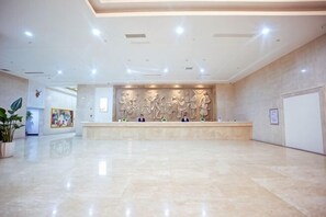 Eine geräumige Lobby mit einer Rezeption, einem großen Wandbild und einer Zimmerpflanze.