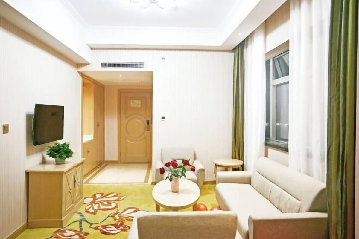 Een hotelkamer met een bank, een tafeltje, een televisie, een kast en een deur naar een andere kamer.