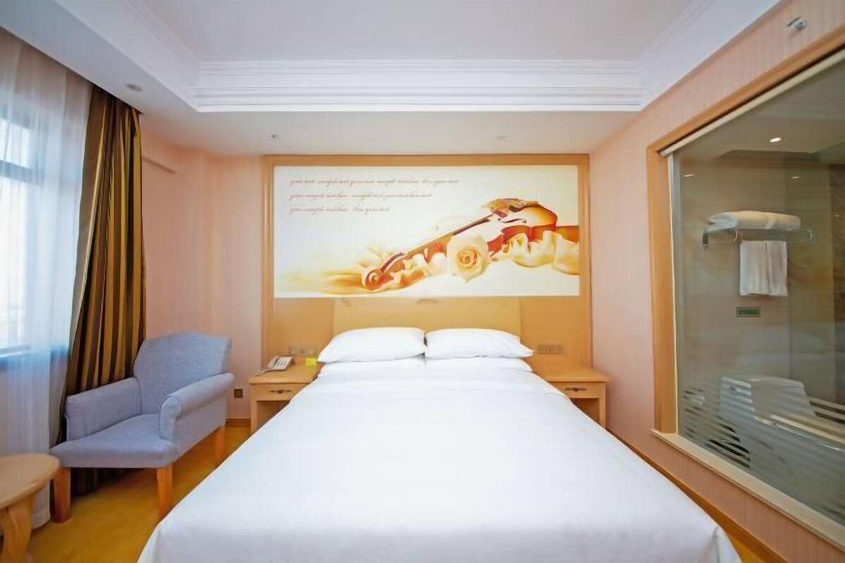 Een hotelkamer met een bed, een stoel, een bureau, een nachtkastje en een groot raam.