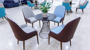 A modern lounge area with a round table surrounded by chairs, a potted plant, and a sofa in the background.