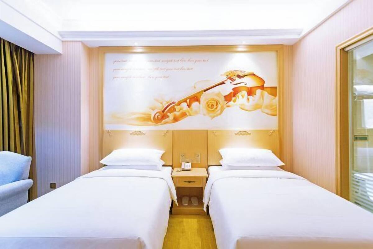 Een hotelkamer met twee bedden, een groot muurdecor en een raam met gordijnen.