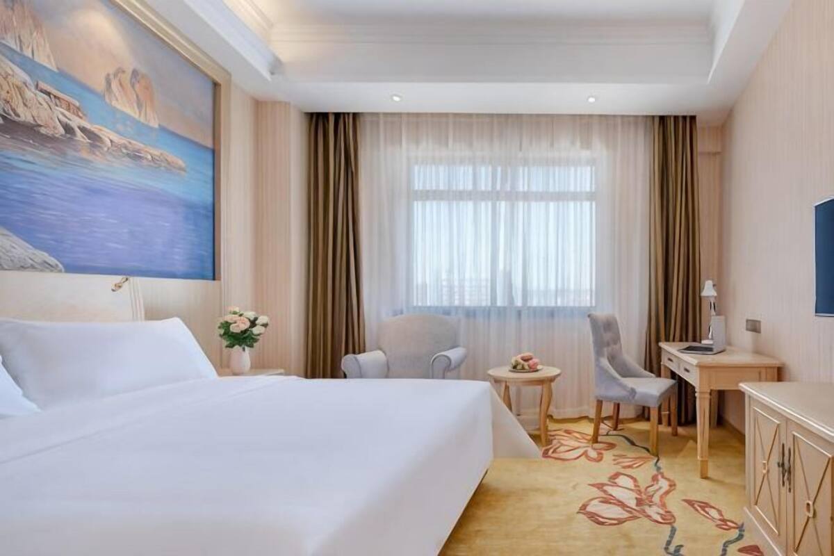 Een hotelkamer met een groot bed, een bureau, een stoel en een klein tafeltje met een bloevas.