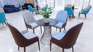 A modern lounge area with a round table surrounded by six chairs, a potted plant, and a mix of blue and brown chairs. - Vienna Hotels Zao Zhuang QingTAN Road (Zaozhuang)