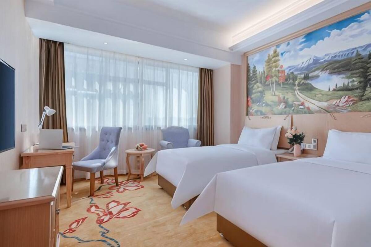 Een hotelkamer met twee bedden, een bureau, een stoel, een kleine tafel en een schilderij aan de muur.