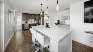 A modern kitchen with a marble island, bar stools, pendant lighting, and stainless steel appliances.