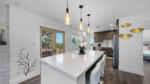A modern kitchen with a marble island, pendant lights, and a view to the outdoors.