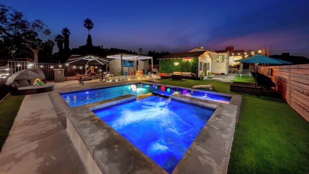A swimming pool with a built-in waterfall feature, surrounded by a patio area with seating and a covered outdoor kitchen.
