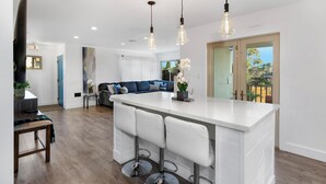 A modern kitchen with a central island, bar stools, pendant lighting, and a view to the outside.
