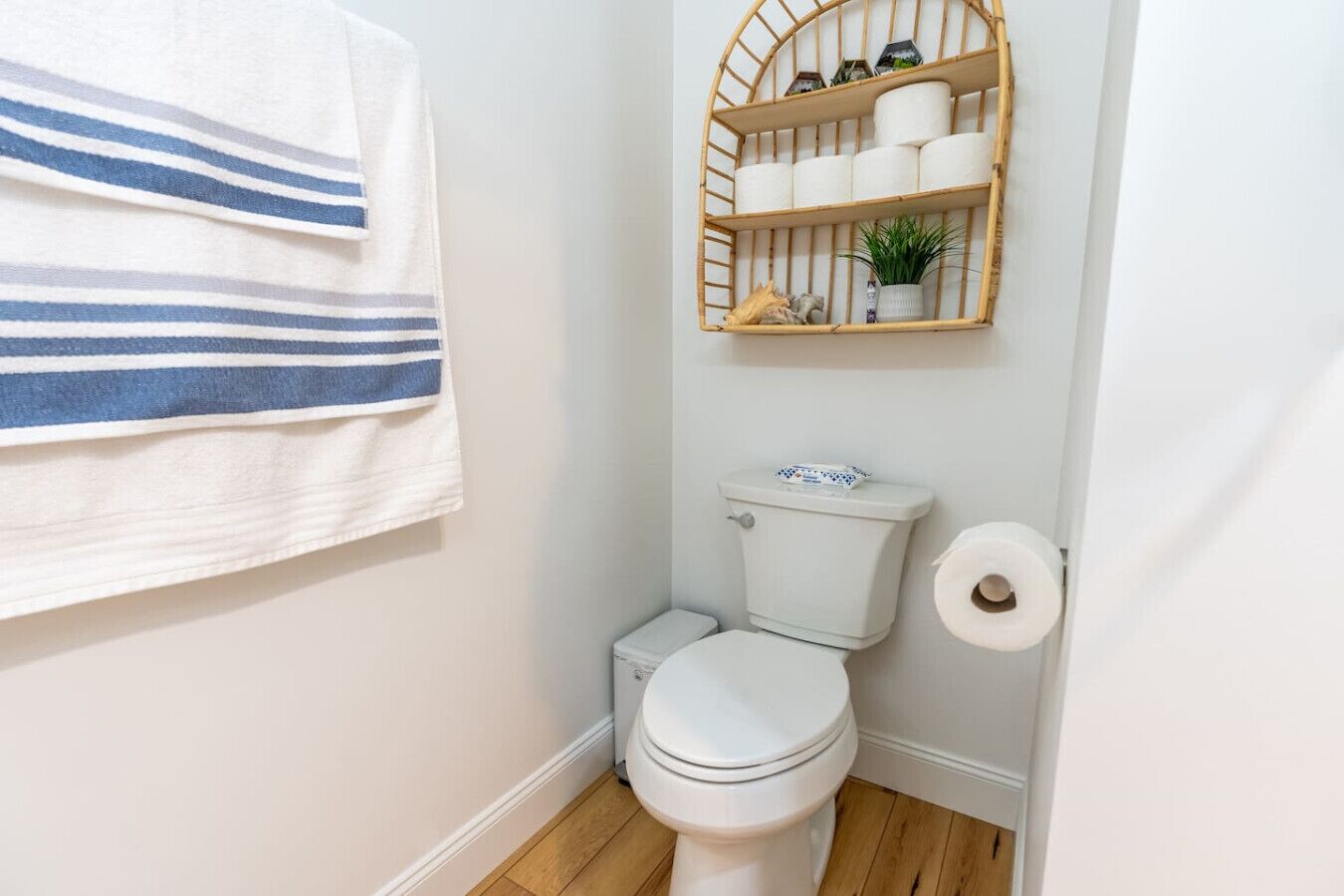 A small bathroom with a toilet, a roll of toilet paper, a striped towel, and a shelf with toiletries.