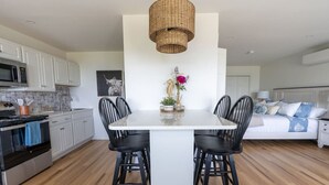 A modern kitchen with white cabinets, a central island, black chairs, and a hanging light fixture. - Lone Star Lodge - Newly Renovated Studio (Northport)